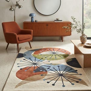 May include: A rectangular area rug featuring a cream-coloured background with a large-scale abstract pattern of overlapping circles and starburst shapes in shades of burnt orange, sage green, slate blue, and dark charcoal grey with textured pile.