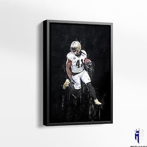 May include: Framed artwork featuring a football player in a white and gold uniform, number 41, running with the ball. The image has a dark, textured background and is set in a black frame. The artwork is signed by MCwallArtUS.