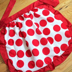 May include: A red and white polka dot apron with a red ruffle around the bottom and a red tie.