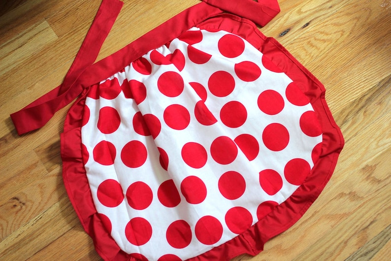 May include: A red and white polka dot apron with a red ruffle around the bottom and a red tie.