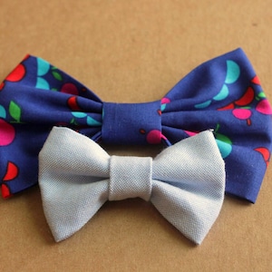May include: Two bow ties, one blue with a colorful fruit pattern and one light blue.