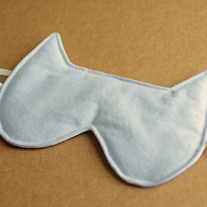 May include: A light blue sleep mask shaped like a cat's head with a white elastic band.