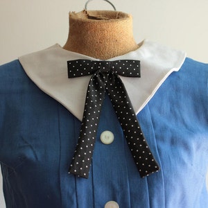 May include: A blue sleeveless dress with a white Peter Pan collar and a black bow tie with white polka dots.