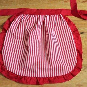 May include: A red and white striped apron with a ruffled edge and a red tie.