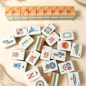 May include: A collection of rectangular mahjong tiles featuring white faces with colorful illustrations of bamboo, flowers, birds, and Chinese characters, alongside a row of stacked tiles with a mottled brown and green layered design.