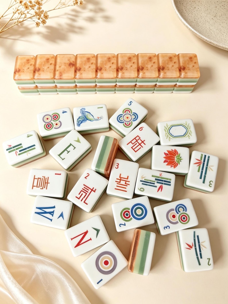 May include: A collection of rectangular mahjong tiles featuring white faces with colorful illustrations of bamboo, flowers, birds, and Chinese characters, alongside a row of stacked tiles with a mottled brown and green layered design.