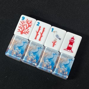 K&ouml;nnte beinhalten: Vier rechteckige Mahjong-Spielsteine mit einem wei&szlig;en oberen Bereich, der nautische und korallenartige Grafiken zeigt, darunter ein roter Korallenzweig mit der Zahl 9, zwei rote Korallenzweige mit der Zahl 2, eine M&ouml;we mit der Zahl 1 und ein Leuchtturm.
