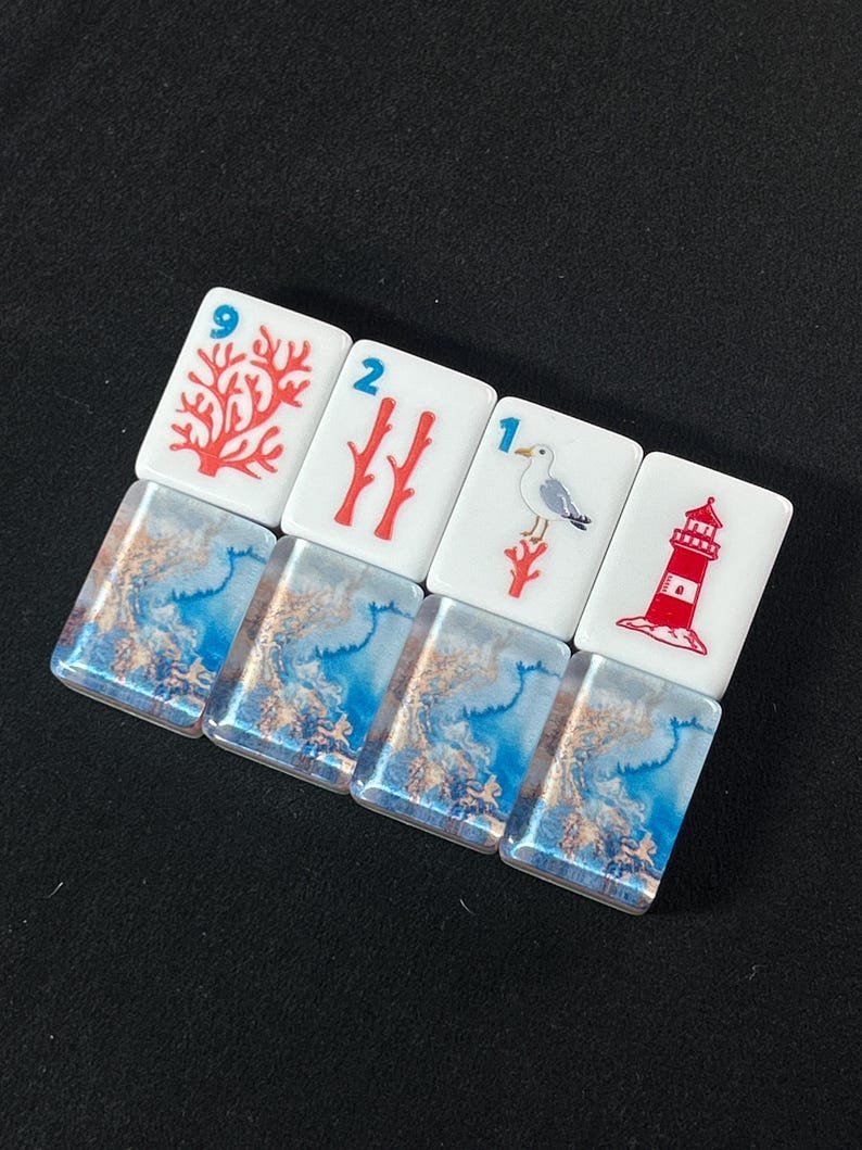 K&ouml;nnte beinhalten: Vier rechteckige Mahjong-Spielsteine mit einem wei&szlig;en oberen Bereich, der nautische und korallenartige Grafiken zeigt, darunter ein roter Korallenzweig mit der Zahl 9, zwei rote Korallenzweige mit der Zahl 2, eine M&ouml;we mit der Zahl 1 und ein Leuchtturm.