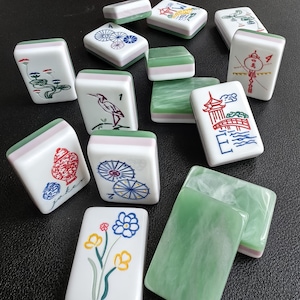 May include: A collection of rectangular Mahjong tiles featuring white faces with colorful illustrations of flowers, birds, pagodas, and umbrellas, alongside green and white marbled backs. Some tiles display the text Joker, 1, 2, and 4.