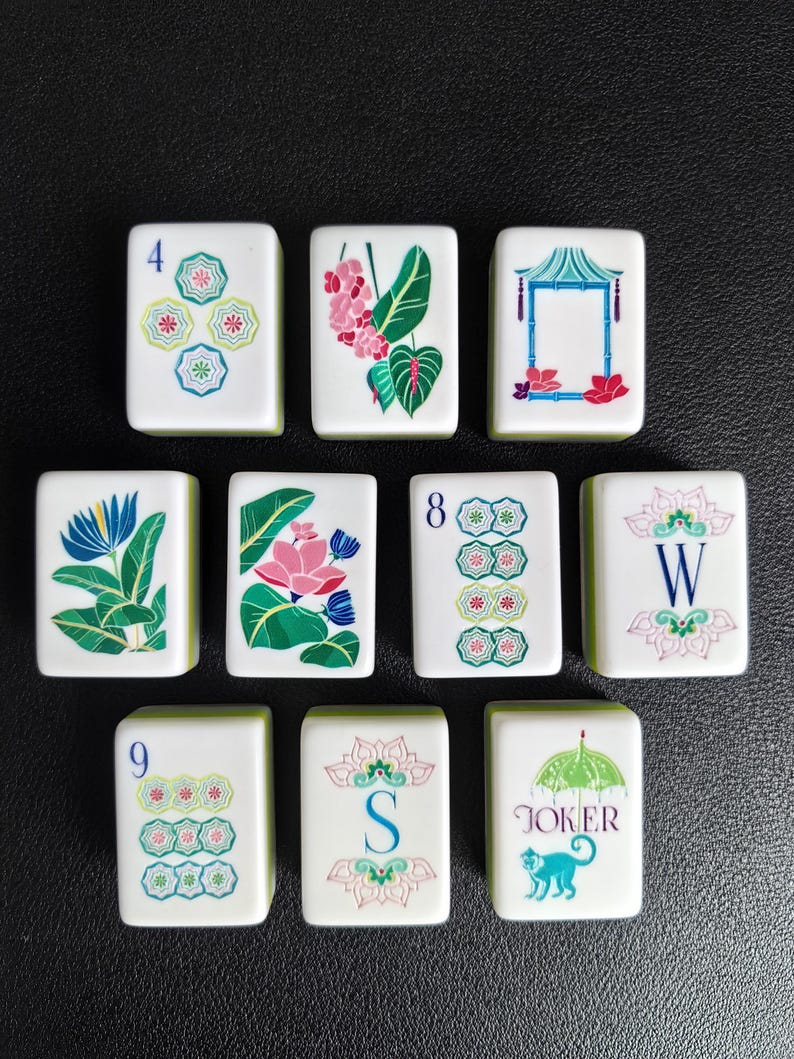 Puede incluir: Un conjunto de diez fichas de mahjong rectangulares blancas con ilustraciones bot&aacute;nicas, florales y geom&eacute;tricas coloridas. Las fichas muestran los n&uacute;meros 4, 8 y 9, las letras W y S, una pagoda, un mono con un paraguas y la palabra JOKER.