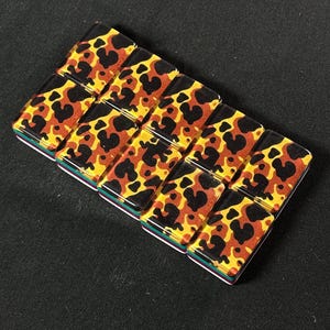 Op de afbeelding: Een rechthoekige armband bestaande uit tien kleine, gladde, rechthoekige tegeltjes gerangschikt in twee rijen. Elk tegeltje heeft een glanzende, doorschijnende afwerking met een luipaardprint in tinten zwart, bruin en goudgeel.
