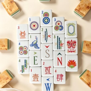 May include: A collection of rectangular mahjong tiles with white faces featuring colorful illustrations of bamboo, circles, characters, and directional letters. The tiles have a marbled tan and green back, arranged in a central cluster.