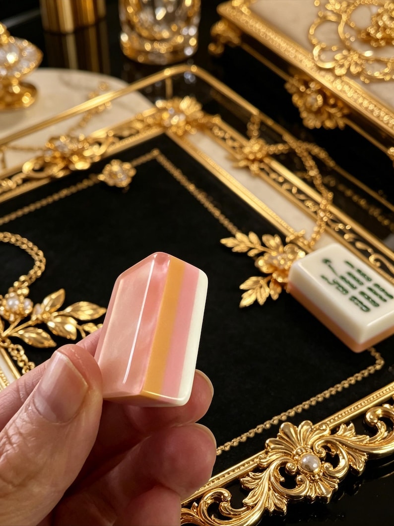 May include: A rectangular mahjong tile featuring a smooth, tri-colored surface with vertical stripes of translucent pink, solid orange, and opaque white. The tile has rounded edges and a polished finish, presented against a black velvet tray.