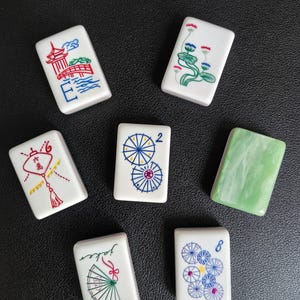 May include: Seven rectangular mahjong tiles with white surfaces and colorful illustrations including a red pagoda, lotus flowers, a red lantern with Chinese characters, blue umbrellas, a green marbled tile, a fan, and blue floral patterns.