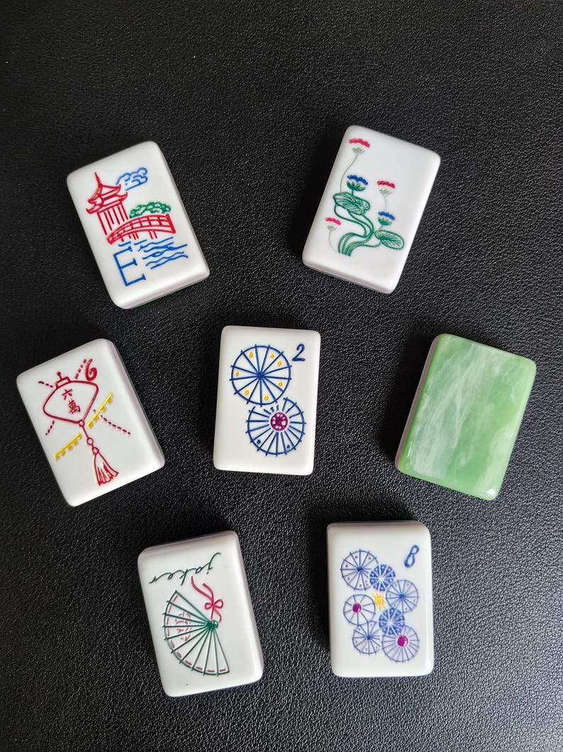 May include: Seven rectangular mahjong tiles with white surfaces and colorful illustrations including a red pagoda, lotus flowers, a red lantern with Chinese characters, blue umbrellas, a green marbled tile, a fan, and blue floral patterns.