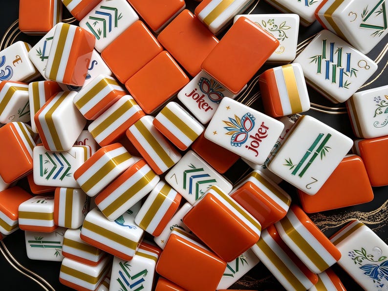 K&ouml;nnte beinhalten: Eine Sammlung rechteckiger Mahjong-Spielsteine mit einer Mischung aus einfarbigen orangefarbenen R&uuml;ckseiten und wei&szlig;en Vorderseiten. Die wei&szlig;en Fl&auml;chen zeigen verschiedene bunte Illustrationen, darunter gr&uuml;ne Bambusstangen, Blumenmuster und Joker-Steine.
