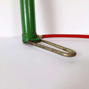 May include: Close-up of a vintage green bicycle pump with a red hose. The pump has a metal foot rest and a green cylinder. The hose is red with a black pattern.