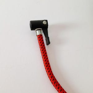 May include: A black air chuck with a lever and a red and black braided hose. The hose is connected to the chuck with a silver metal fitting. The image is taken against a white background.
