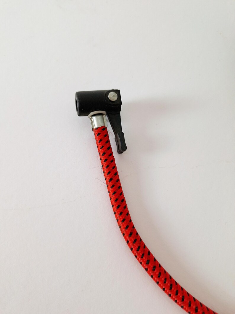 May include: A black air chuck with a lever and a red and black braided hose. The hose is connected to the chuck with a silver metal fitting. The image is taken against a white background.