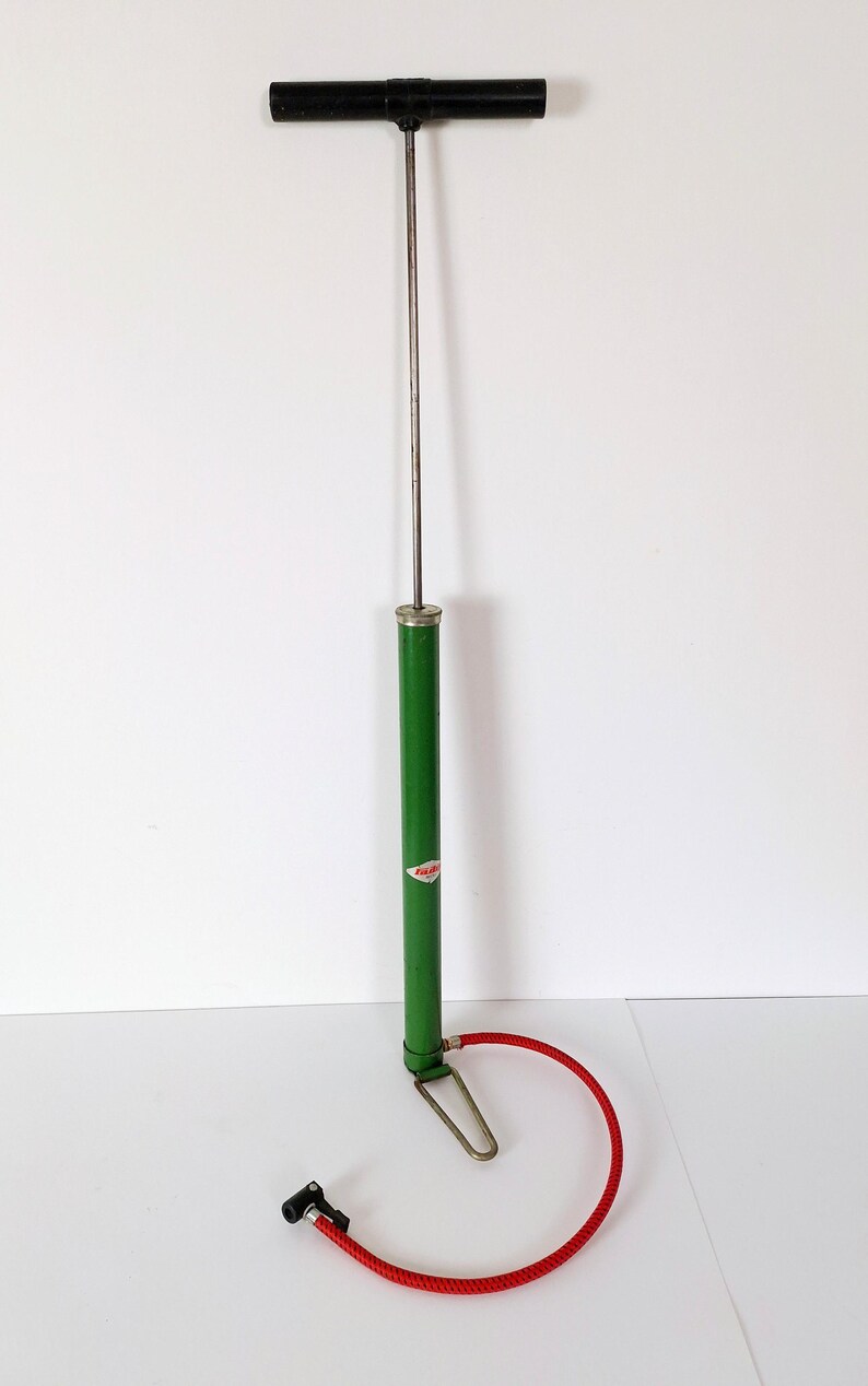 May include: A vintage bicycle pump with a black handle and a green body. The pump has a silver metal shaft and a red hose with a black nozzle. The pump is designed for inflating bicycle tires.