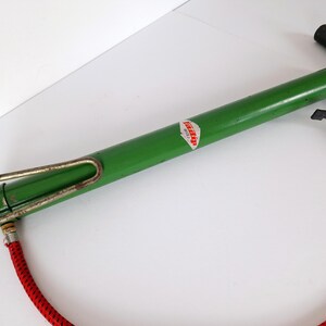May include: A vintage green bicycle pump with a black handle and a red hose. The pump has a metal frame and a label with the word "Tipp" on it. The pump is designed to inflate bicycle tires.
