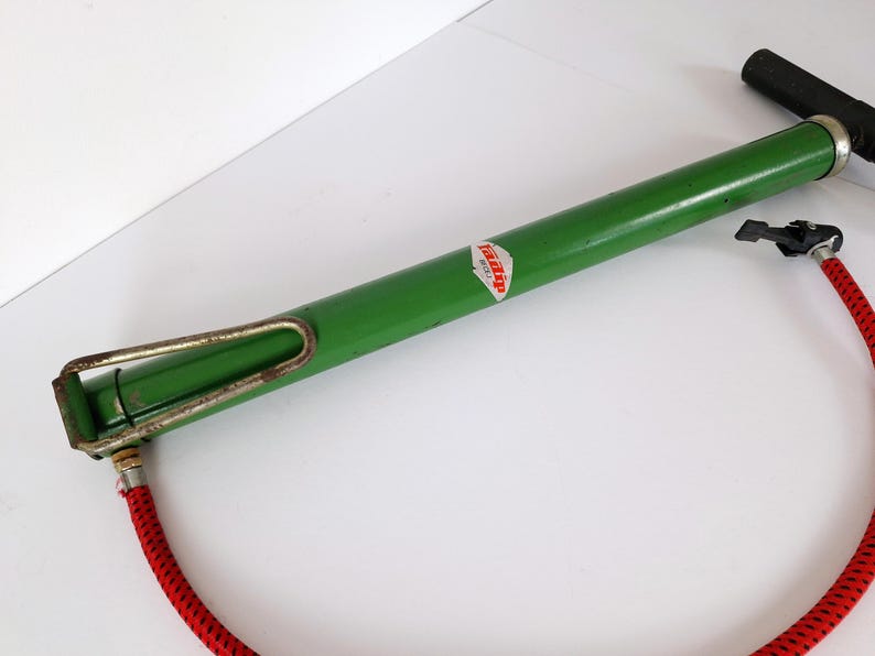 May include: A vintage green bicycle pump with a black handle and a red hose. The pump has a metal frame and a label with the word "Tipp" on it. The pump is designed to inflate bicycle tires.