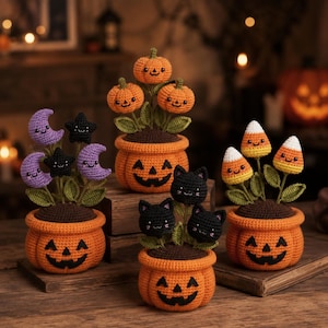 Könnte beinhalten: Eine Sammlung von vier gehäkelten Halloween-Pflanzen in Töpfen. Jeder orangefarbene Topf hat ein aufgesticktes Kürbisgesicht. Die Pflanzen bestehen aus gehäkelten lila Monden, schwarzen Sternen, orangefarbenen Kürbissen, schwarzen Katzen und Zuckermais.