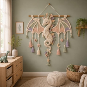 Peut inclure: Une décoration murale en macramé représentant un dragon couleur crème avec de grandes ailes multicolores dans des tons vert sauge, rose poudré et lavande. L'objet est suspendu à une tige en bois et comporte des pompons, des étoiles et des cœurs.