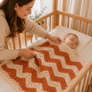 May include: A crochet baby blanket featuring a chevron pattern in alternating stripes of cream and burnt orange yarn. The blanket has a scalloped edge and is made with a textured stitch, providing a soft and decorative covering for a sleeping infant.