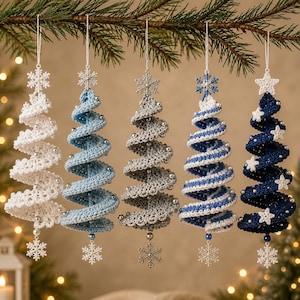 Könnte beinhalten: Fünf spiralförmige Weihnachtsbaum-Anhänger aus Häkelarbeit, die in einer Reihe hängen. Die Bäume sind weiß, hellblau, silber, blau-weiß gestreift und dunkelblau. Jeder ist mit kleinen silbernen Perlen sowie einem Stern oder Schneeflocken verziert.