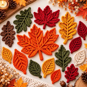 May include: A collection of crocheted autumn leaves in various shapes and sizes, featuring colours of red, orange, yellow, brown, green, and cream. The leaves include maple and oak designs with visible yarn textures and central vein details.