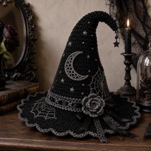 May include: A black crocheted witch hat featuring a silver crescent moon, spider web embroidery, and small star accents. The hat is adorned with a crocheted rose, black satin ribbons, and a dangling star charm at the pointed tip.