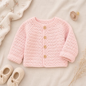May include: A light pink long-sleeved crochet cardigan featuring a round neckline and four small, round, light brown wooden buttons down the center front. The garment is crafted with a textured stitch pattern and has ribbed cuffs at the wrists.