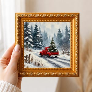 Può includere: Un'opera d'arte murale quadrata in una cornice dorata decorata che raffigura un paesaggio invernale. Il dipinto mostra un pickup rosso brillante che trasporta un albero di Natale decorato lungo una strada innevata tra alberi di pino.