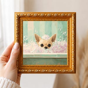 May include: A square painting in a decorative gold frame featuring a tan chihuahua with large dark eyes peeking out from a bathtub filled with white and pink soap bubbles against a light green striped background.
