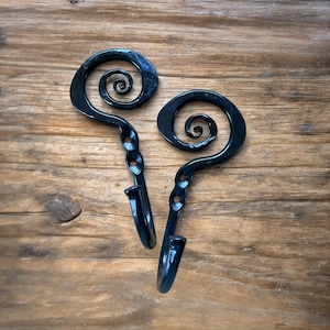 Könnte beinhalten: Zwei schwarze Metallhaken mit Spiraldesign. Die Haken sind auf einer Holzoberfläche montiert.