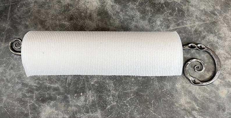May include: A metal paper towel holder with a spiral design. The holder is made of dark metal and has a white paper towel roll on it.