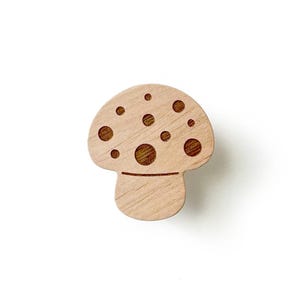 Könnte beinhalten: Ein Wandhaken aus Holz in Form eines Pilzes mit hellbrauner Oberfläche und einem gepunkteten Design.
