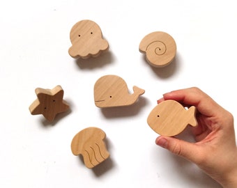 May include: Wooden toy set featuring a whale, octopus, starfish, seashell, and fish. The toys are all made of natural wood and have a light brown color.