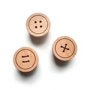 May include: Three wooden buttons with different designs. The first button has four holes, the second button has two parallel lines, and the third button has a cross.