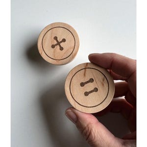 May include: Two wooden buttons with different designs. One button has a cross shape and the other has two parallel lines.