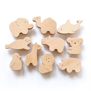 May include: A set of 10 wooden animal figurines, including a camel, elephant, hippopotamus, seal, giraffe, penguin, koala, bear, whale, and rhinoceros. The figurines are all made of natural wood and have a light brown colour.