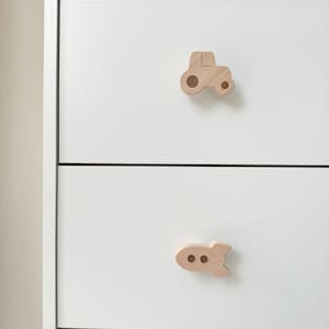 May include: White dresser with two drawers. The top drawer has a wooden tractor knob and the bottom drawer has a wooden rocket ship knob.