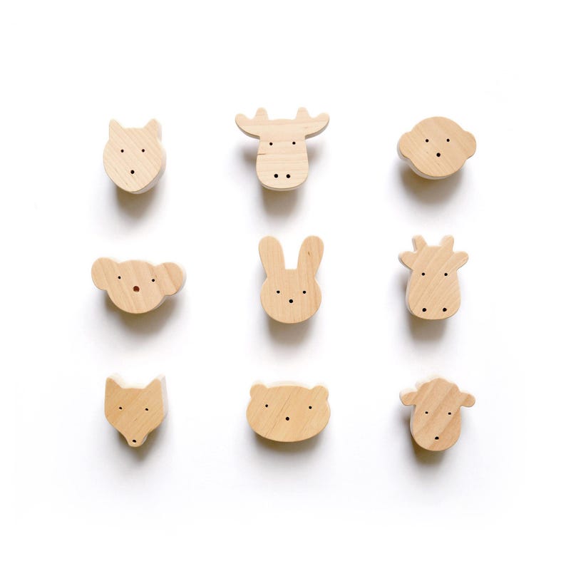 A grid of nine handmade wooden animal drawer knobs on a white background, featuring bear, moose, bunny, and fox shapes for nursery decor.
