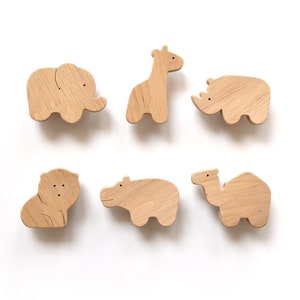 Könnte beinhalten: Sechs Holzfiguren von Tieren, darunter ein Elefant, eine Giraffe, ein Nashorn, ein Löwe, ein Flusspferd und ein Kamel. Die Figuren sind alle aus hellem braunem Holz gefertigt und haben einfache, cartoonartige Designs.