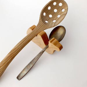 May include: Wooden camel-shaped spoon holder with a slotted wooden spoon and a silver spoon.