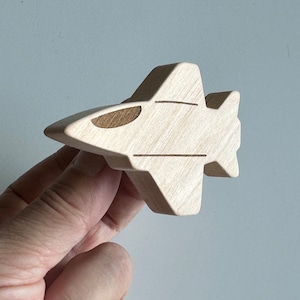 May include: A wooden toy airplane in a light brown color. The airplane has a simple design with a rounded nose and wings.