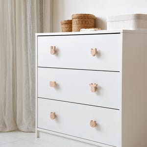 White nursery dresser featuring wooden forest animal knobs, including bunny, fox, bear, and moose shapes, in a bright and cozy room.