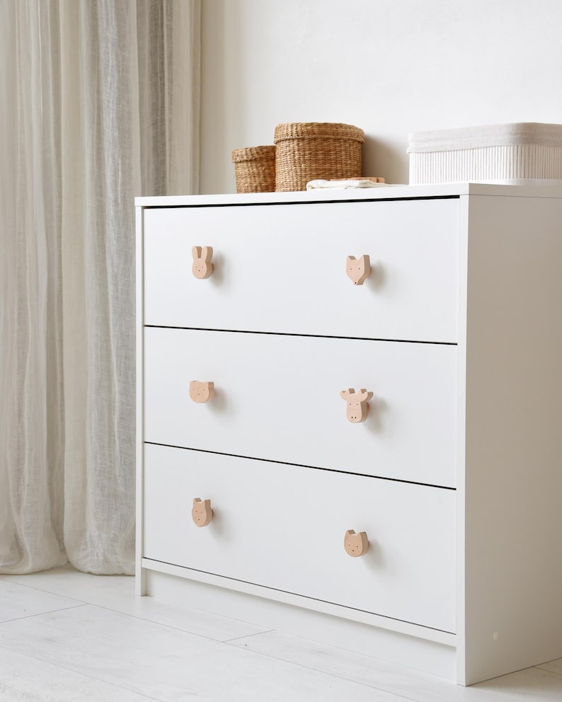 White nursery dresser featuring wooden forest animal knobs, including bunny, fox, bear, and moose shapes, in a bright and cozy room.