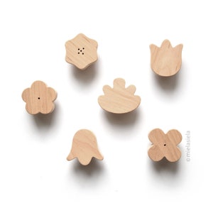 May include: Five wooden wall hooks shaped like flowers. The hooks are in the shape of a tulip, a five-petal flower, a four-petal flower, a flower with a rounded center, and a star-shaped flower.